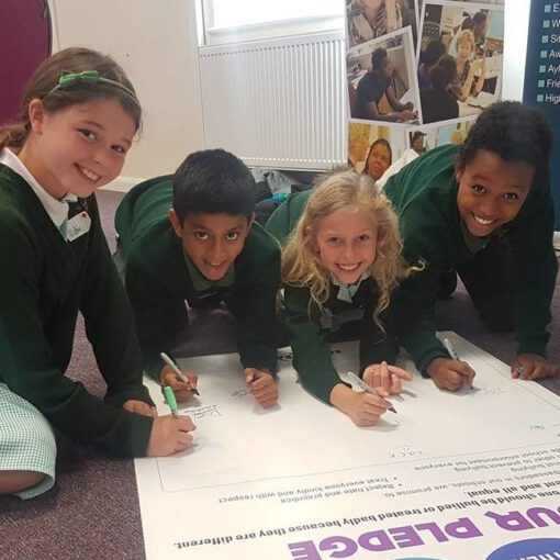 4 smiling primary pupils signing an EqualiTeach pledge, promising to tackle bullying in their school.