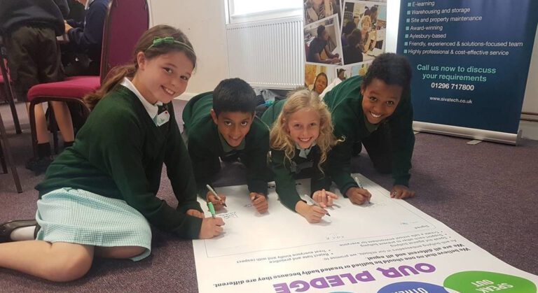 4 smiling primary pupils signing an EqualiTeach pledge, promising to tackle bullying in their school.